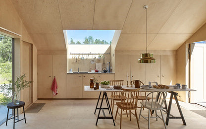 Lifestyle inspiration: a bright kitchen and dining space finished in natural birch plywood, showing the wood grain on walls, ceiling and cabinets.